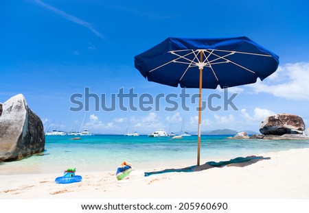 Picture perfect beach with blue umbrella, white sand, turquoise ocean water and blue sky at tropical island in Caribbean