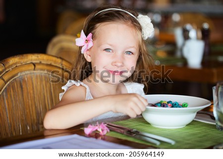 Adorable little girl eating cereal with milk for breakfast in restaurant