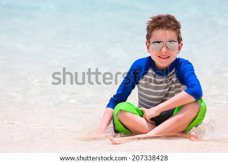 Cute little boy in sun protection rash guard at tropical beach on summer vacation