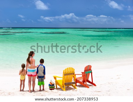 Family of mother and kids enjoying vacation at tropical beach with two colorful wooden chairs on white sand and turquoise ocean water in Caribbean