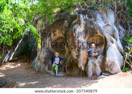Little kids on a huge rock that looks like face or skull at The Baths trail major tourist attraction at Virgin Gorda, British Virgin Islands, Caribbean