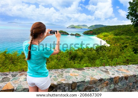 Back view of tourist girl taking photo with mobile cell phone of Trunk bay on St John island, US Virgin Islands considered by many as most beautiful beach in Caribbean