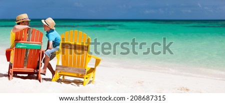 Father and son family sitting on colorful wooden chairs at tropical beach enjoying summer vacation panorama perfect for banners