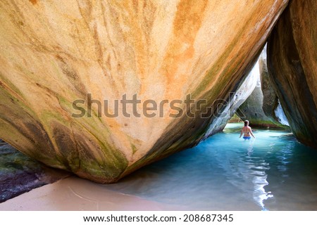 Young girl at cave covered with water at The Baths beach area major tourist attraction at Virgin Gorda, British Virgin Islands with white sand, turquoise ocean and huge granite boulders