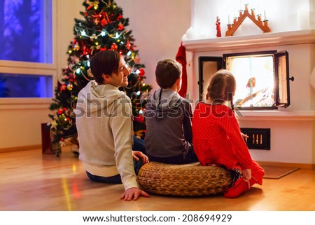 Father and his two little kids sitting by a fireplace in their family home on Christmas eve