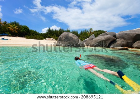 Young woman in sun protection swimwear snorkeling in turquoise tropical water at exotic island beach