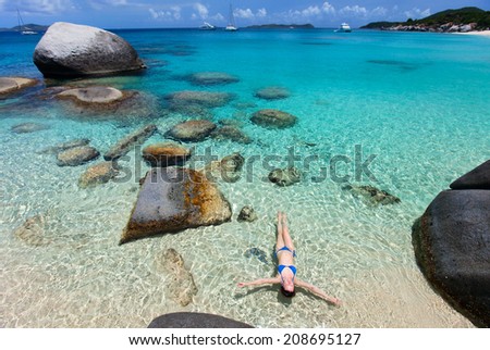 Above view of beautiful young woman relaxing floating in turquoise tropical water among granite boulders at Virgin Gorda, BVI, Caribbean