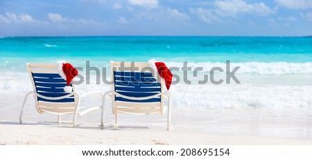 Two sunloungers with Santa hats on beautiful tropical beach with white sand and turquoise water, perfect Christmas vacation