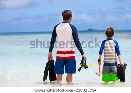 Back view of father and son with snorkeling equipment fins and mask at tropical beach