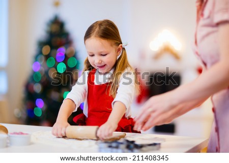 Family of mother and daughter baking Christmas gingerbread cookies at home on winter day