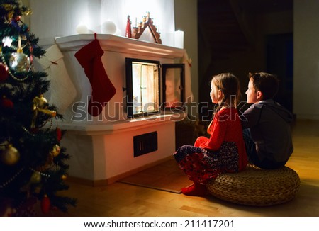 Two little kids sitting by a fireplace at home on Christmas eve