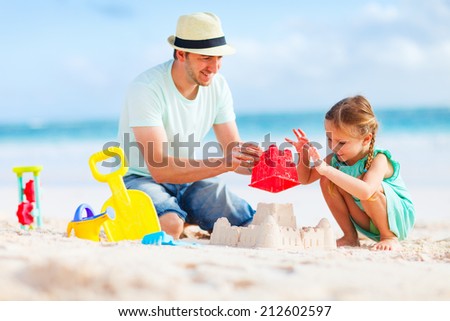 Father and daughter on beach playing and building sand castle