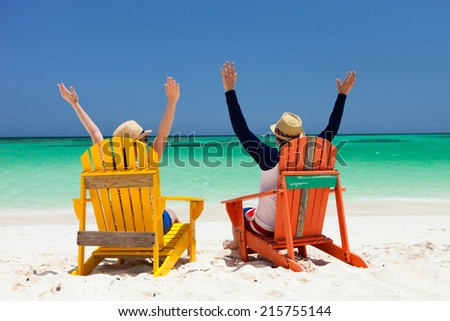 Happy couple sitting on colorful chairs at tropical beach enjoying Caribbean vacation