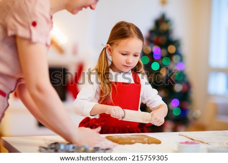 Family of mother and daughter baking gingerbread cookies at home on Christmas eve