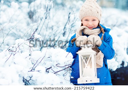 Adorable little girl holding Christmas lantern outdoors on beautiful winter snow day