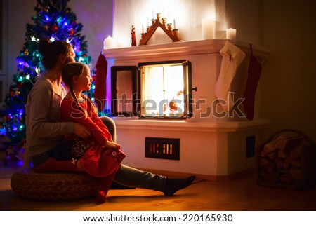 Mother and daughter sitting by a fireplace in their family home on Christmas eve