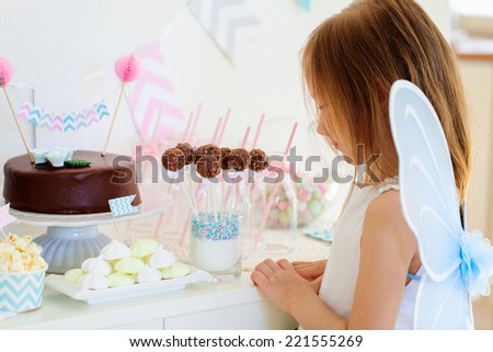 Adorable little fairy girl with wings on a birthday party near dessert table