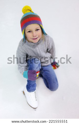 Adorable little girl wearing jeans, warm sweater and colorful hat skating on ice rink