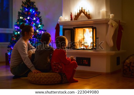 Mother and her two little kids sitting by a fireplace in their family home on Christmas eve