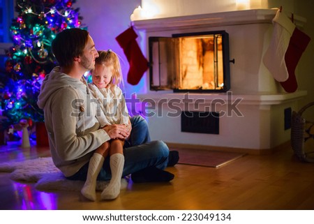 Father and daughter sitting by a fireplace in their family home on Christmas eve