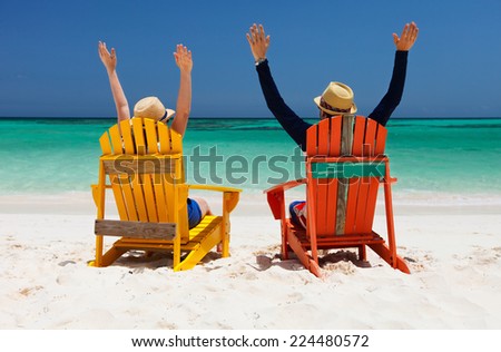Happy couple sitting on colorful chairs at tropical beach enjoying Caribbean vacation