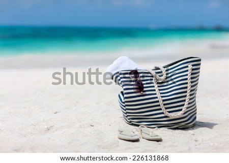 Bag with beach towel, sun glasses and flip flops on a tropical beach