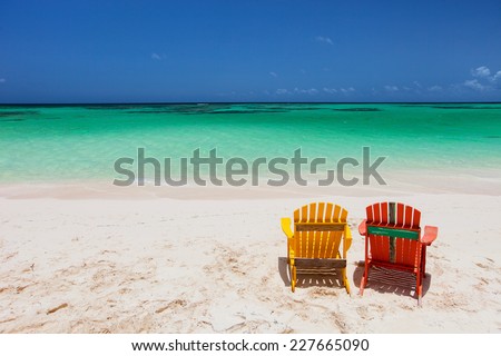 Colorful adirondack yellow and orange lounge chairs at tropical beach in Caribbean with beautiful turquoise ocean water, white sand and blue sky