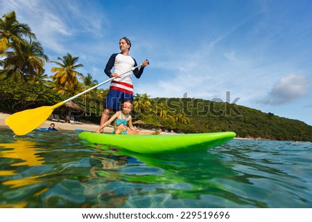 Father and his adorable little daughter paddling on stand up board having fun during summer beach vacation
