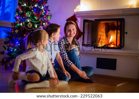 Family of mother and her two little kids sitting by a fireplace in their home on Christmas eve