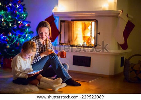 Family of mother and daughter sitting by a fireplace in their home on winter