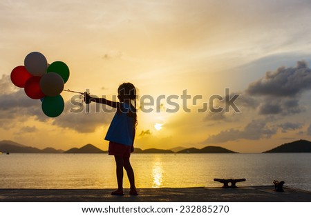 Silhouette of adorable happy little girl with bunch of balloons on sea coast at sunset