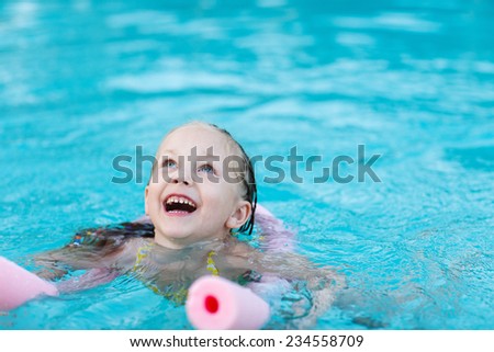 Adorable little girl swimming with a pink foam noodle in a pool while on summer vacation
