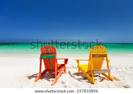 Colorful yellow and orange lounge chairs at tropical beach in Caribbean with beautiful turquoise ocean water, white sand and blue sky