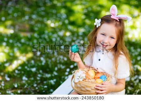Above view of adorable little girl wearing bunny ears playing with Easter eggs on a grass covered with white flower petals on spring day