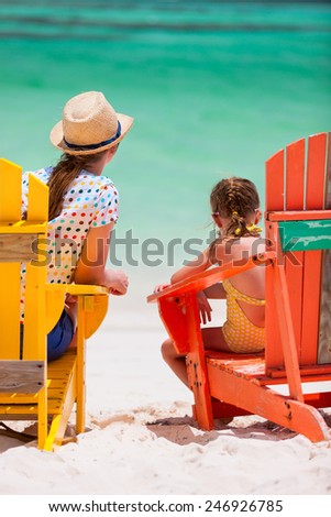 Back view of mother and daughter family sitting on colorful wooden chairs at tropical beach enjoying summer vacation