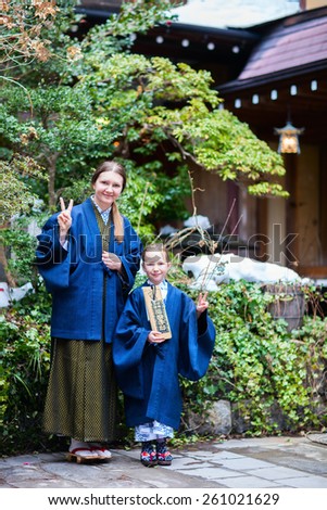 Family mother and daughter wearing traditional Japanese kimono at street of onsen resort town in Japan. Translation of text on wooden plate: passport for round bath visit to protect you from bad luck.