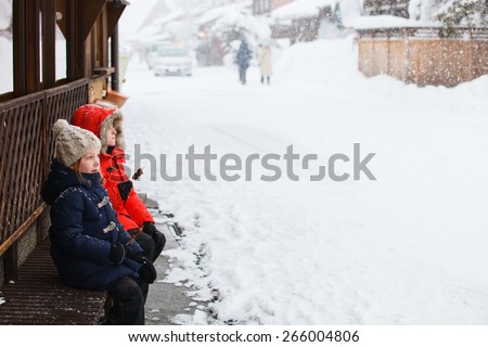Kids eating hida beef snack outdoors on winter day at historical village of Shirakawa-go in Japan