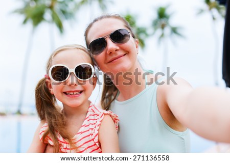 Happy family mother and her adorable little daughter on summer vacation taking selfie with smartphone