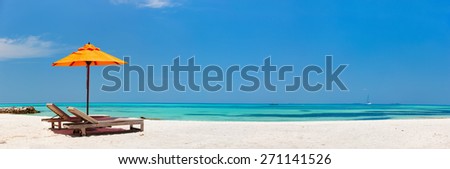 Wooden lounge chairs and orange sun umbrella on a beautiful tropical beach at Maldives
