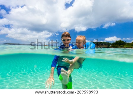 Split underwater photo of adorable little girl and cute boy splashing in a tropical ocean water during summer vacation