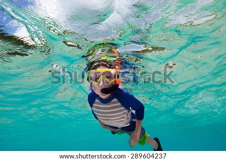 Cute teenage boy swimming underwater in shallow turquoise water at tropical beach