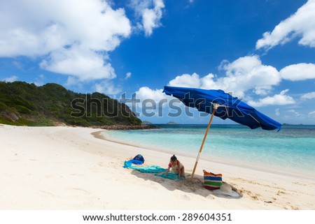 Little girl on picture perfect beach with blue umbrella, white sand, turquoise ocean water and blue sky at tropical island in Caribbean