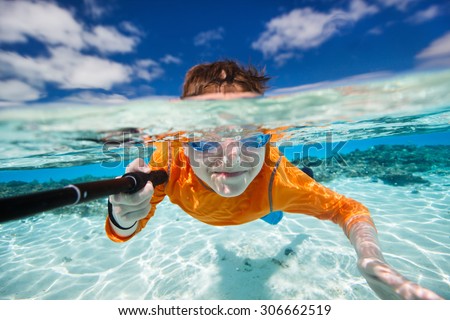 Cute teenage boy making selfie underwater in shallow turquoise water at tropical beach