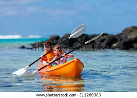 Kids enjoying paddling in colorful red kayak at tropical ocean water during summer vacation