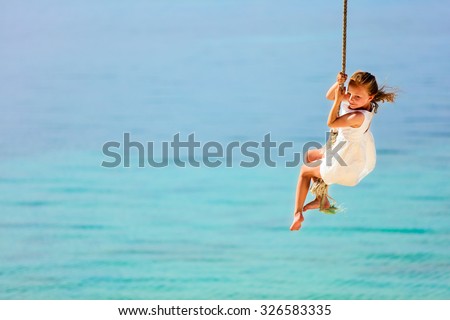 Little girl having fun swinging on a rope at tropical island beach