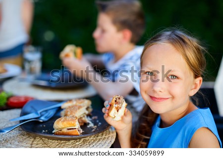 Adorable little girl and her family eating delicious homemade burger outdoors on summer day