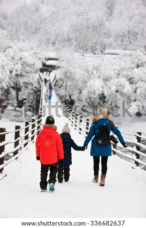 Family of mother and kids crossing the bridge over Shogawa river at historic Japanese village Shirakawa-go at winter, one of Japan\'s UNESCO world heritage sites