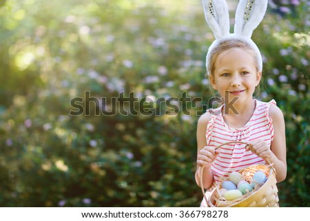 Adorable little girl wearing bunny ears holding a basket with Easter eggs outdoors on spring day