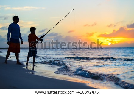Father and son fishing together in ocean from beach on sunset