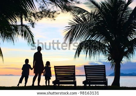 Silhouettes of mother and two kids at sunset on tropical island